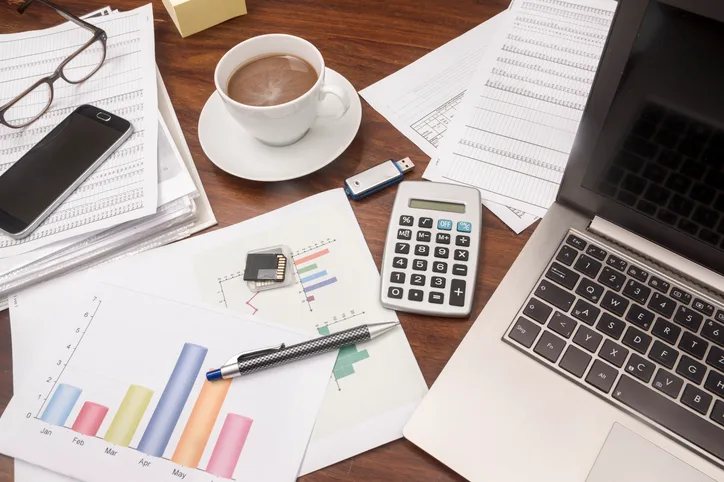 Desk with charts, a calculator, coffee and a laptop