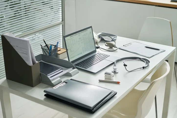 Medical office desk with a laptop, files and a stethoscope