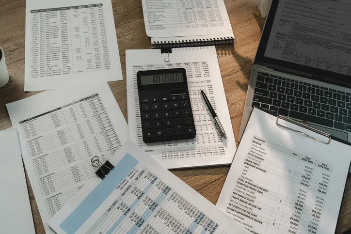 Financial statements, calculator and laptop spread on a desk