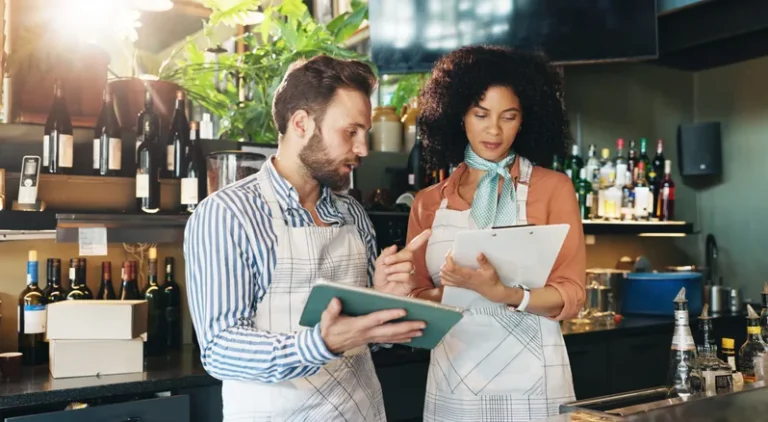 Two restaurant owners reviewing records on a tablet and clipboard
