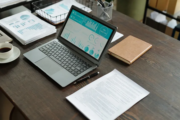 Laptop showing a financial dashboard on a desk with reports